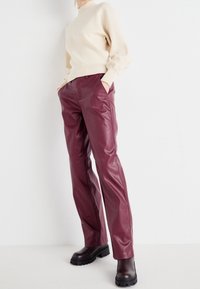 Pull en maille beige avec des poignets côtelés, associé à un pantalon en cuir bordeaux. Le mannequin porte des bottes chelsea à semelle épaisse noires.