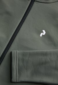Olivgrön blixtlåsförsedd jacka med svart dragkedja, med en liten vit logotyp. Slät textur med åtsittande mudd och sömdetaljer.