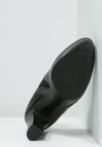 Botte cheville en cuir noir avec une tête ronde, semelle en caoutchouc dotée de motifs de grip circulaires et un panneau élastique pour plus de flexibilité. Taille 37 indiquée sur la semelle.