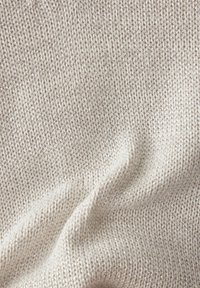 Hellbeige, strukturiertes Strickgewebe mit einem subtilen Glanz. Eingewebte metallische Fäden schaffen eine weiche, einladende Oberfläche und ein zartes Muster.