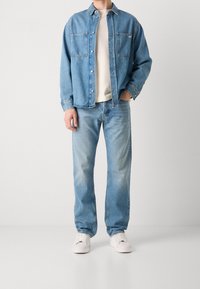 Světle modrá džínová košile se dvěma náprsními kapsami, spárovaná se světle modrými džíny. Bílí tenisky dotvářejí outfit.