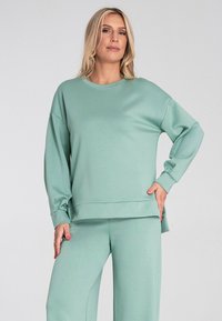 Miętowozielony, oversize sweter z długimi rękawami i okrągłym dekoltem. Miękka faktura, z luźnym krojem i bocznymi rozporkami dla komfortu.