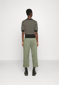 Czarny dzianinowy sweter z geometrycznym wzorem, krótkie rękawy, w zestawieniu z zielonymi szerokimi spodniami i czarnymi masywnymi botkami.