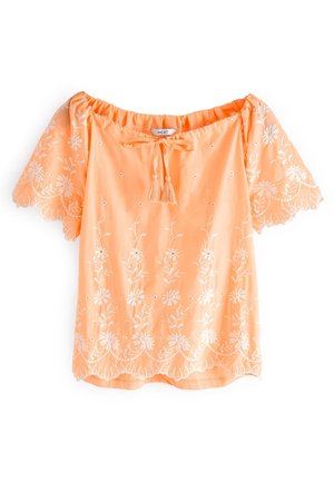 Blouse pêche à manches courtes avec broderie florale blanche, bords festonnés et petit lien à pompons à l'encolure froncée.