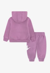 Σετ με ροζ φούτερ με κουκούλα και παντελόνι φόρμας, κατασκευασμένο από απαλό ύφασμα. Διαθέτει τσέπη μπροστά, ελαστικά τελειώματα και μεγάλο λευκό λογότυπο στο παντελόνι.