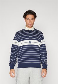 Navy and white striped long-sleeve polo with a collar and logo. Features ribbed cuffs and hem. Worn with gray sweatpants.