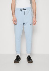 Light blue jogger pants made of soft fabric, featuring an elastic waistband with drawstring, ribbed cuffs, and black logo detail.