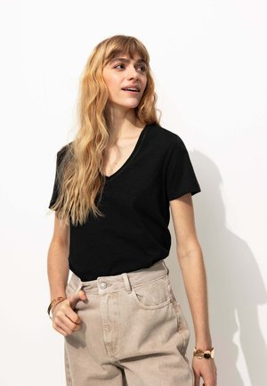 T-shirt noir à col en V fabriqué en tissu doux, associé à un pantalon beige taille haute. Présente une coupe décontractée et des manches courtes.