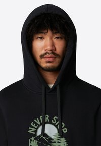 Sort hættetrøje med snoretræk i huen, med et grønt trykt design af bjerge og teksten "NEVER STOP" på brystet. Blød tekstur.