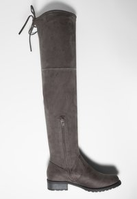 Bota de ante gris oscuro alta con cremallera lateral, tacón bajo y costuras decorativas en el tobillo y en la parte superior, con un lazo en la parte posterior.