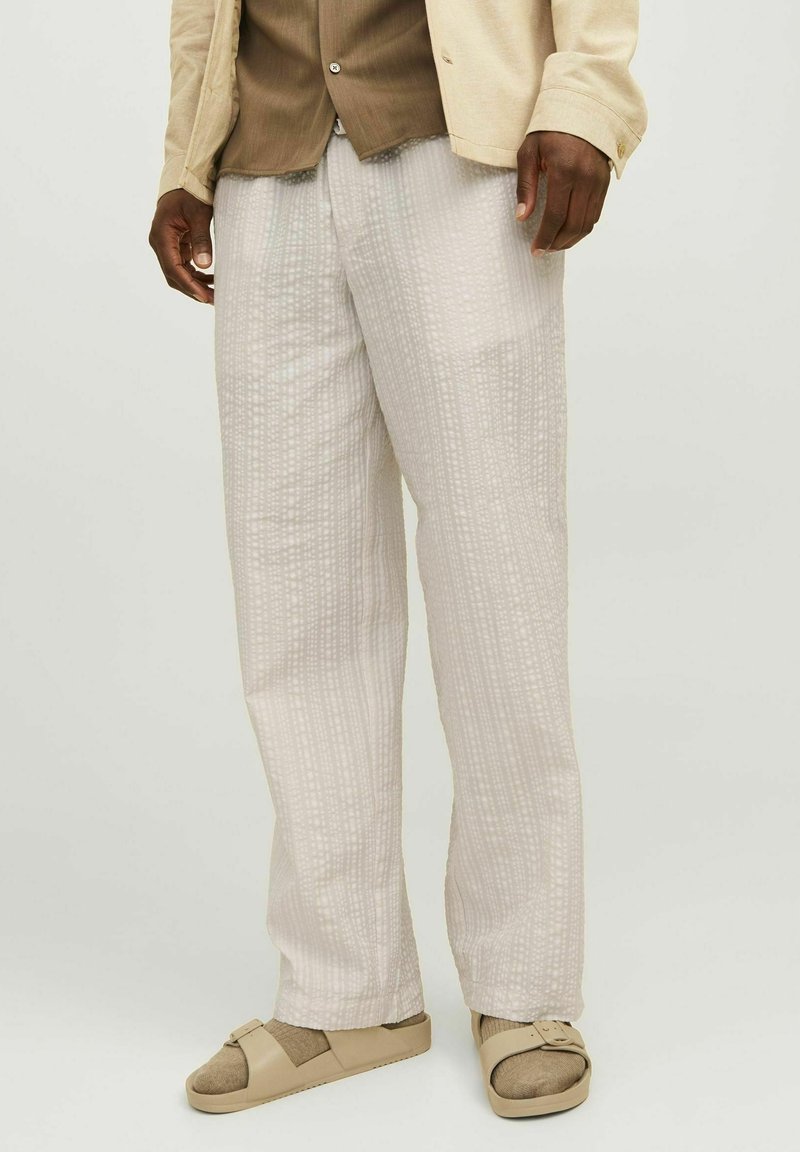 Pantalones de lino de color claro y textura, con un diseño de patrón sutil, combinados con sandalias beige. Corte suelto y relajado, adecuado para un uso casual.