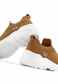 Sneakers slip-on con una toma in maglia marrone, suola in gomma bianca, texture rigata e nappo, con un discreto dettaglio del logo.