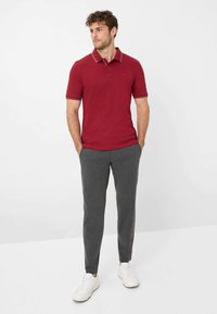 Rød polo T-shirt med hvid trim, parret med grå skræddersyede bukser og hvide sneakers. Poloen har en knappet krave og kortærmer.