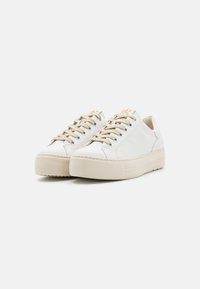 Baskets en cuir blanc avec une semelle crème épaisse, dotées de lacets dorés et d'un détail de texte subtil sur la languette. Design à bout rond.