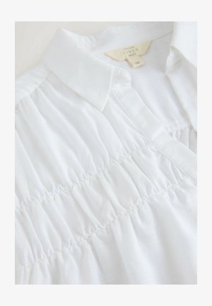 Bílá lněná košile s límečkem, s nabráním na předním díle, jemnou texturou a jednoduchými designovými prvky.