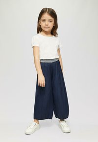 Witte t-shirt met korte mouwen en een bloemenaccent, gecombineerd met marineblauwe geplooide culottes met een sprankelende tailleband en witte sneakers.