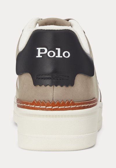 Tył beżowego sneakersa z białą podeszwą, brązowym paskiem ze skóry, czarną zakładką na pięcie oraz białym logo „Polo” na pięcie.