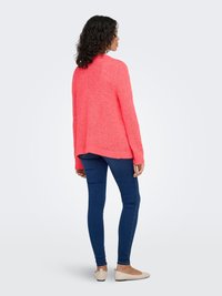 Bright coral knit sweater with a relaxed fit, paired with dark blue skinny jeans and light flats. Sweater features a textured finish and long sleeves.