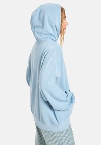 Ljusblå hoodie med avslappnad passform, som har en stor huva, ribbad mudd och nederkant. Mjuk textur, bärs tillsammans med mönstrade byxor.