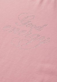 Roze stof met zilveren studs die de cursieve tekst "Glamour Couture" in een decoratieve stijl vormen.