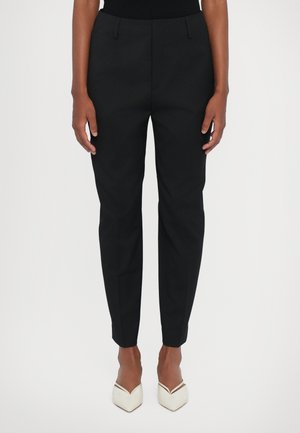 Svarta skräddarsydda byxor med slim fit, med sidfickor, en mjuk tygtextur och en kortare längd, i kombination med vita klackskor.
