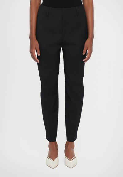 Pantalons noirs ajustés avec une coupe slim, dotés de poches latérales, d'une texture de tissu lisse et d'une longueur raccourcie, associés à des chaussures blanches à talons.