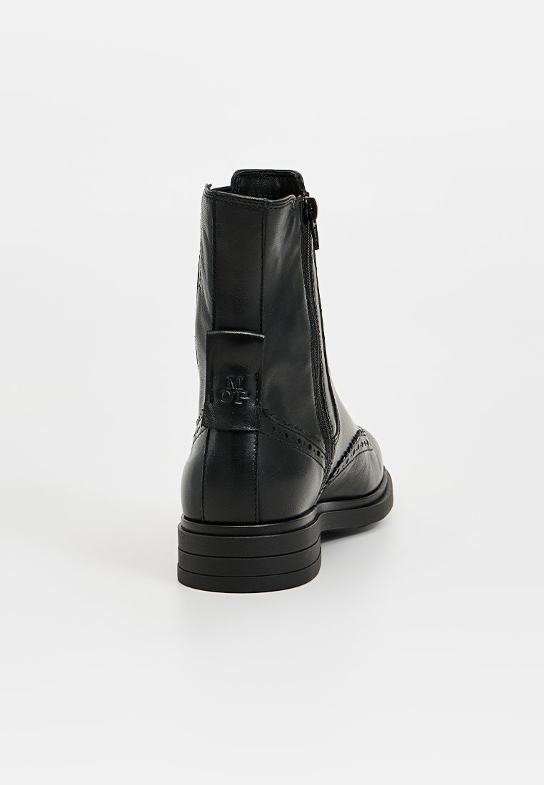 Zwarte leren enkellaars met een gestructureerde bovenkant, ritssluiting aan de achterkant en een lage gestapelde hak. Voorzien van decoratieve brogue-details.
