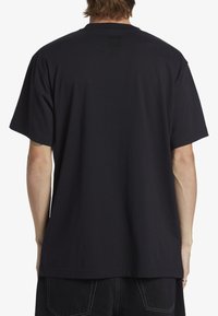 Svart bomullströja med korta ärmar, rund halsringning och en avslappnad passform. Har en enfärgad baksida och minimal sömnadsdetalj.