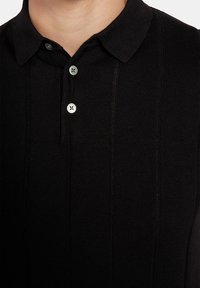 Czarna koszulka polo z kołnierzykiem, krótkimi rękawami, trzyguwkową zapięciem oraz drobną prążkowaną strukturą; zawiera pionowe detale w szwie.