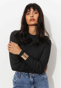 Chemise noire à manches longues avec une finition texturée, assortie à un jean en denim bleu taille haute et un large bracelet en métal.
