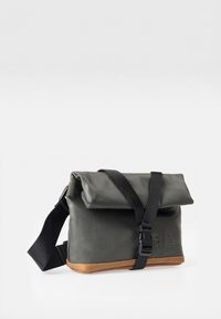 Green waterproof bag with a fold-over flap, black adjustable strap, and brown leather base. Features a simple design and logo detail.