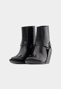 Svarta läderankelstövlar med spetsig tå, vertikal dragkedja och en dekorativ rem med silverfärgade detaljer och accenter.