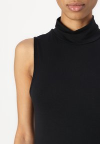Haut sans manches noir à col roulé en matériau doux et extensible avec une texture lisse. Présente un col haut et une silhouette ajustée.