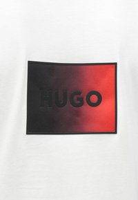 Λευκό κοντομάνικο μπλουζάκι με ένα ορθογώνιο γραφικό που έχει διαβάθμιση από μαύρο σε κόκκινο, με τη λέξη "HUGO" σε έντονα μαύρα γράμματα.