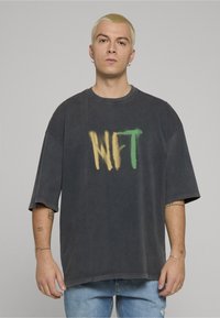 Zwart oversized T-shirt van zacht stof, met een spuitverf "NFT"-print in geel en groen op de voorkant.
