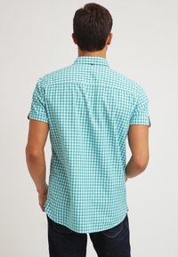 Camisa corta de manga corta a cuadros en turquesa con cuello, con pieza en la espalda y dobladillo curvado; material de algodón con textura suave.