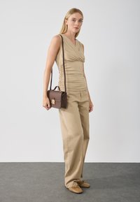 Haut sans manches beige avec des côtés froncés, pantalon large beige assorti et un petit sac à main marron texturé avec un fermoir doré.