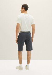 Dunkelblaue Shorts mit einem strukturierten Muster, ausgestattet mit Seiten- und Gesäßtaschen, kombiniert mit einem hellen T-Shirt und Sneakers.