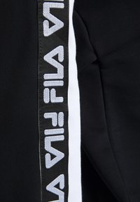 Svarta byxor med en vit sidosträck och grå "FILA"-logotyp. Texturerad tyg med en slät finish och atletisk passform.