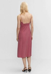 Midi-Kleid in staubigem Rosé, aus weichem Stoff, mit dünnenTrägern, einem gerafften Rücken und einer geraden Silhouette. Getragen mit schwarzen Riemchen-High Heels.