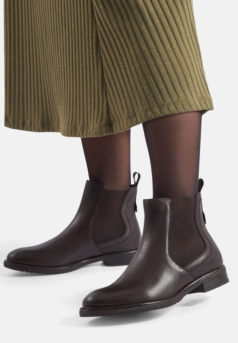 Botines de cuero marrón con paneles laterales elásticos, un tacón bajo apilado y un acabado suave, combinados con una falda de canalé verde.