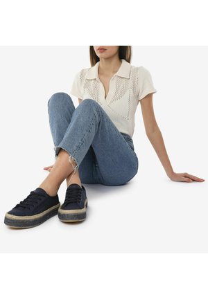 Knit, light beige polo shirt with short sleeves and a collar; worn with medium-wash denim jeans and dark sneakers with a jute sole.
