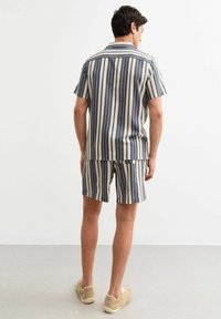 Completo composto da camicia a maniche corte a righe e pantaloni corti nei colori blu navy, beige e crema. Realizzato in morbido tessuto, presenta righe verticali e una vestibilità rilassata.