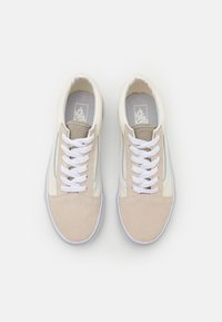 Zapatillas blancas y beige con materiales de ante y lona. Presentan cordones blancos, franjas laterales y un cuello acolchado. Punta redonda y suela plana.