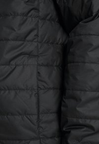 Svart pufferjacka med en slät yta, quiltat mönster och horisontella sömmar. Inkluderar en subtil blixtlåsficka.