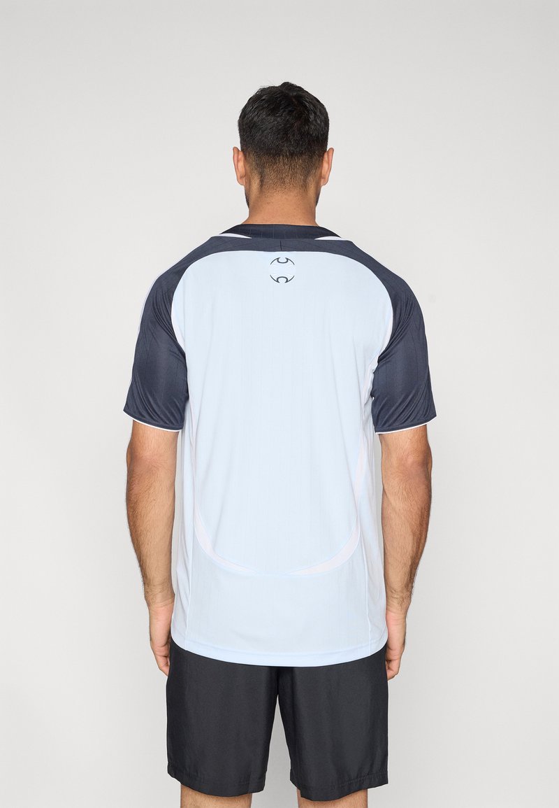 T-shirt de sport bleu clair avec manches bleu foncé, col rond, et texture subtile à rayures verticales. Présente un marquage minimal au dos.