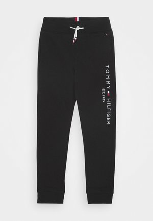 Sorte joggerbukser med ribbet kant, hvid snor og teksten "Tommy Hilfiger EST. 1985" trykt lodret på højre ben.