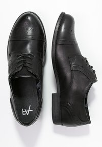 Chaussures habillées en cuir noir avec un bout rond, un design à lacets, des détails perforés et une semelle plate en caoutchouc.