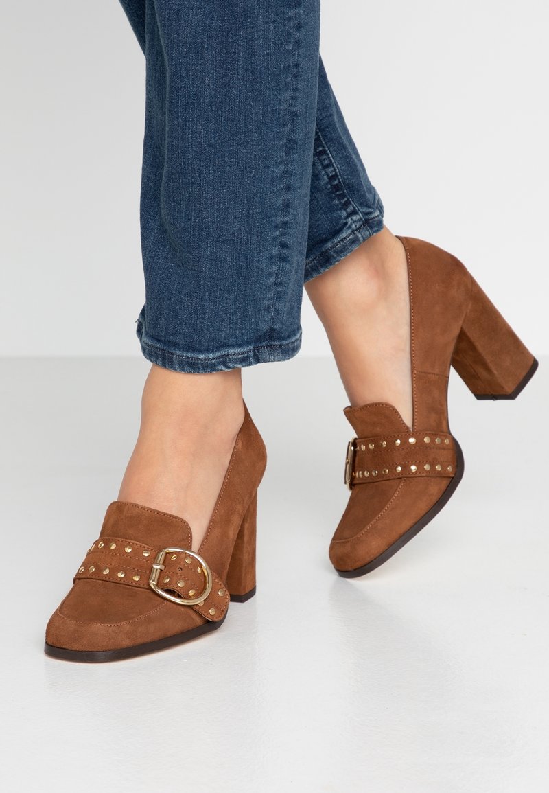 Chaussures à talons hauts en daim marron avec un bout arrondi, dotées d'une large bride ornée de clous dorés et d'un détail décoratif avec boucle.