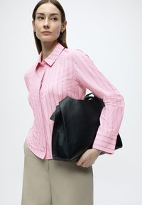 Ροζ ριγέ πουκάμισο με μακρύ μανίκι και γιακά, συνδυασμένο με μπεζ παντελόνι και υφασμάτινη μαύρη τσάντα χειρός. Η τσάντα έχει μοναδικό σχήμα και λαβές.